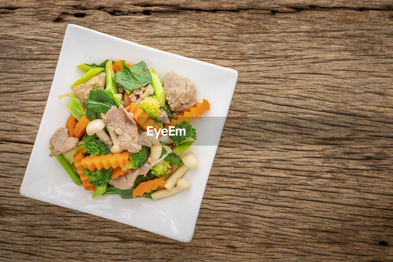 Stir fried mixed vegetables with pork and shimeji mushroom in white square ceramic plate, top view