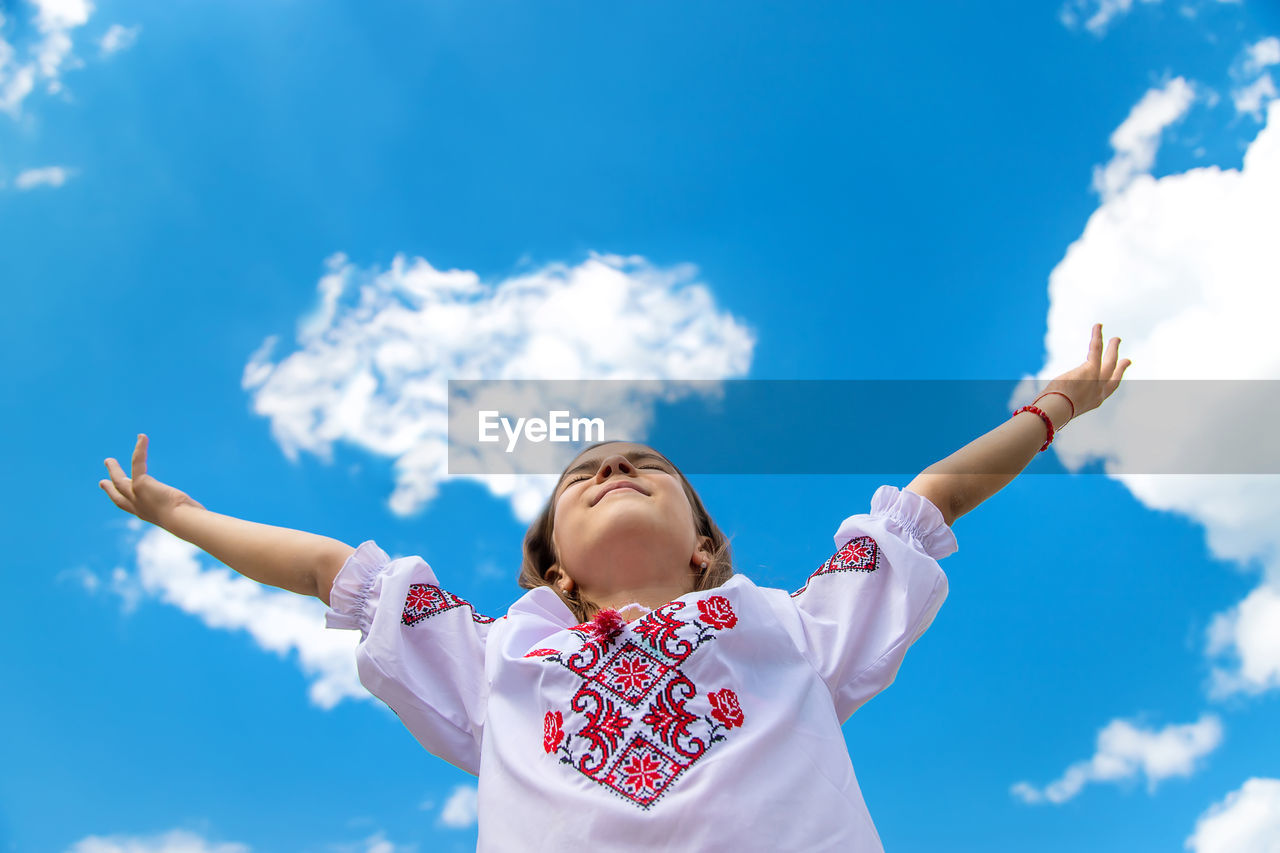 Low angle view of girl with arms raised against sky