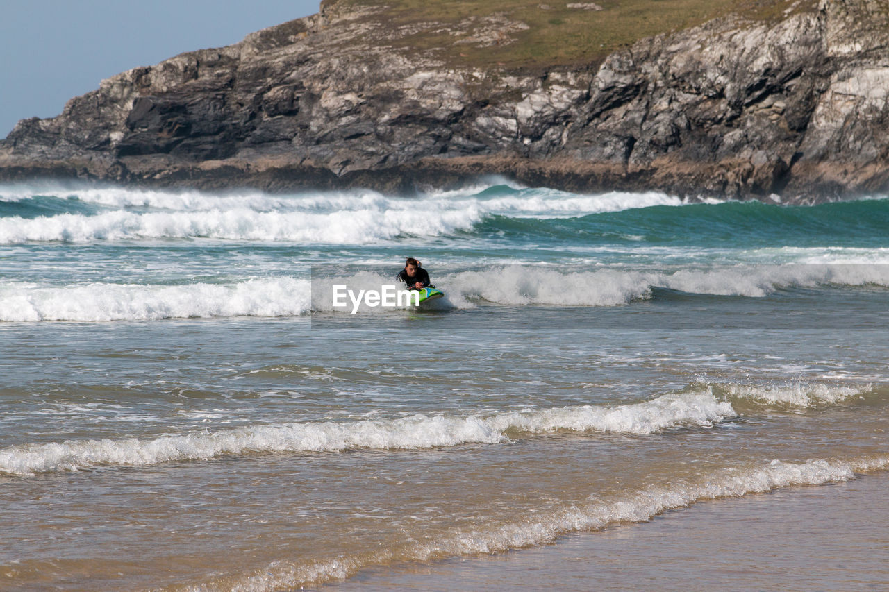 MAN SURFING ON SEA WAVES AT BEACH