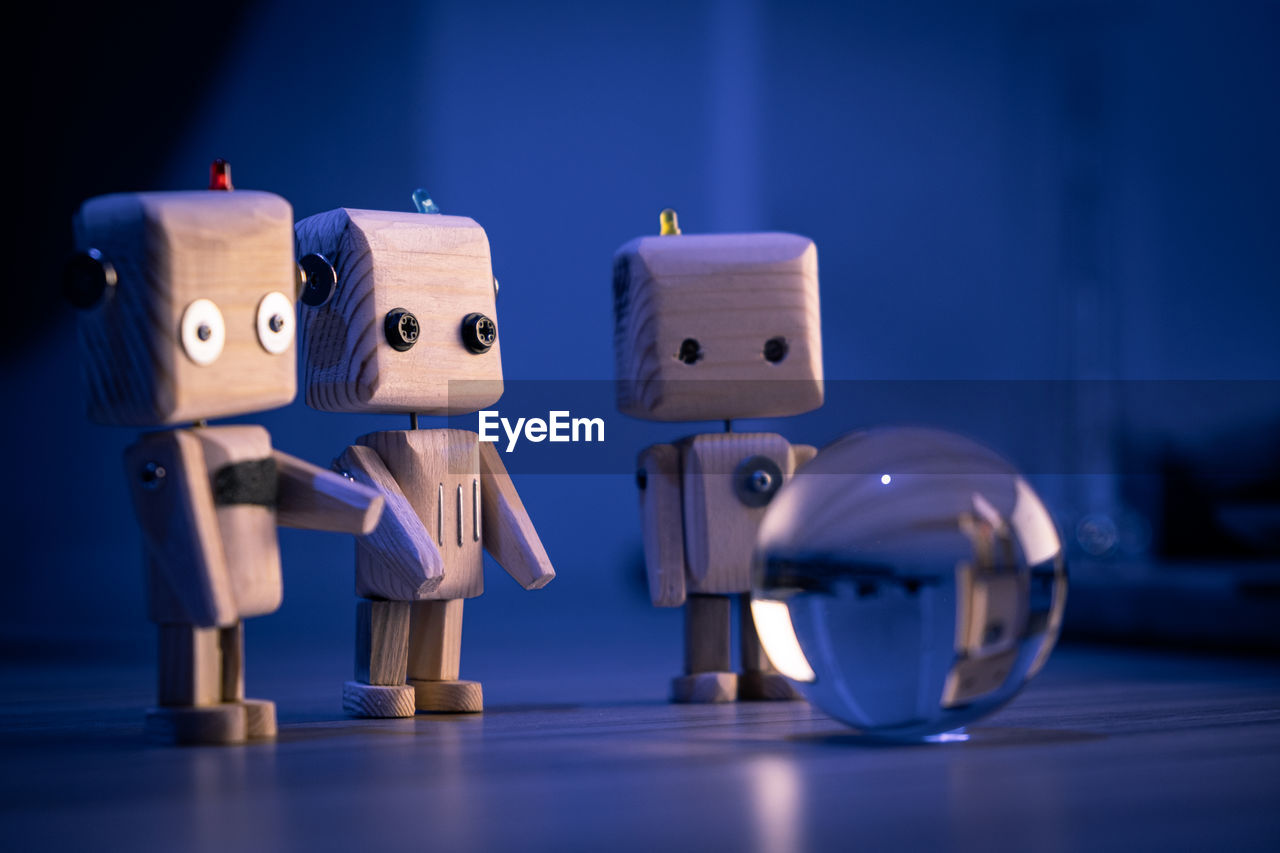 A small wooden toy robots looks at a glass ball in the dark. wallpaper, blured background. low light