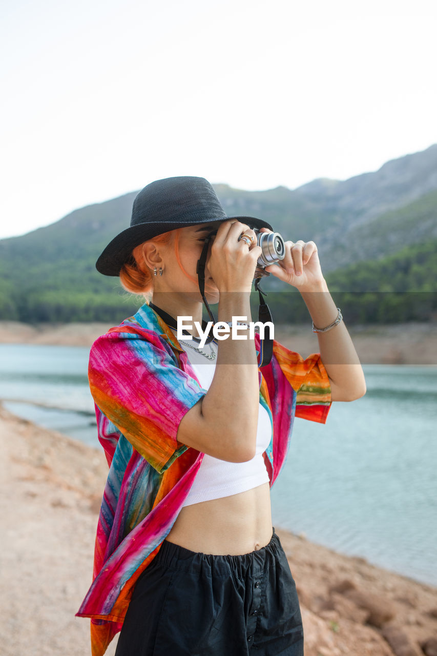 Woman with black hat in a lake taking pictures of the landscape