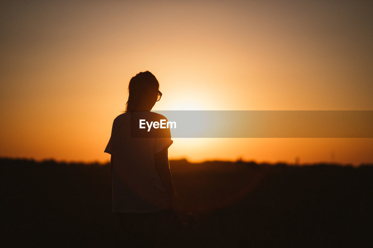 Woman standing on field against sky during sunset