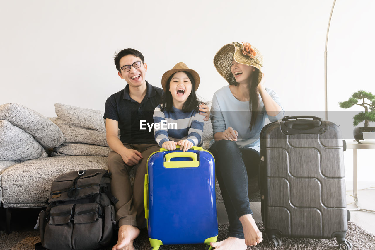 Happy family sitting with luggage on sofa in living room at home