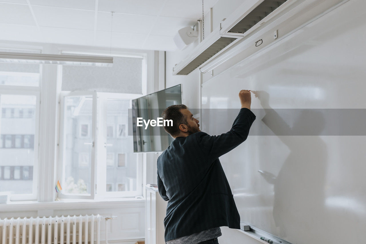 Side view of mature male professor writing on whiteboard in classroom