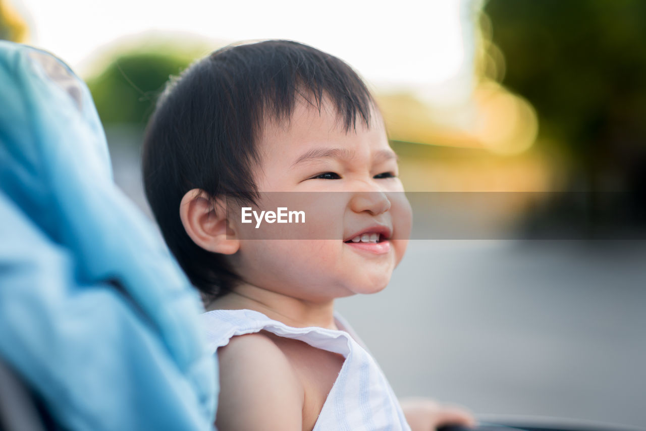 Smiling baby looking away while sitting in carriage outdoors