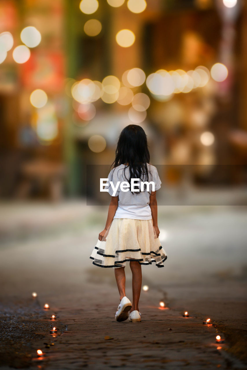 Rear view of girl walking in illuminated city