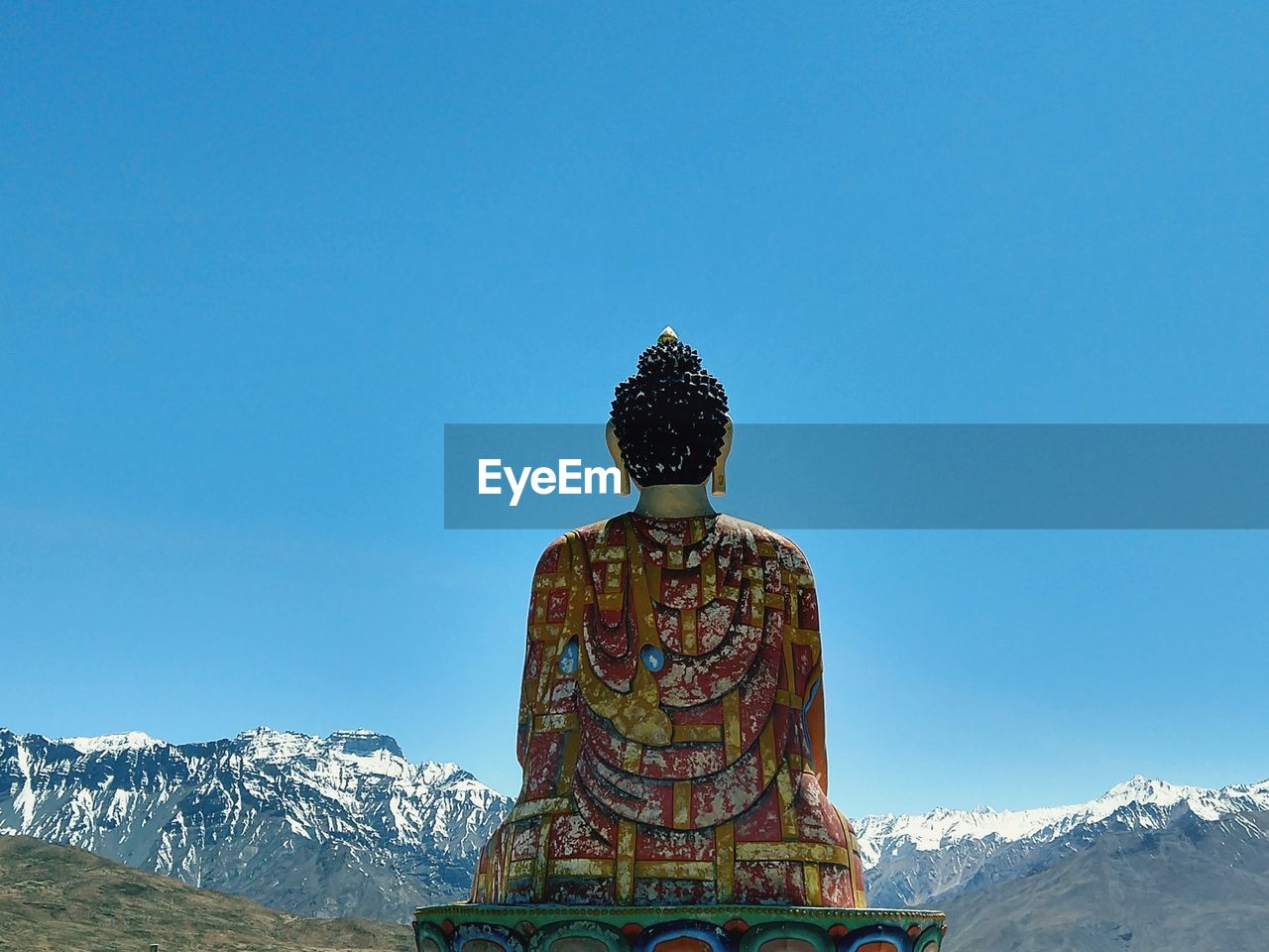 Buddha statue against snowcapped mountains and clear sky