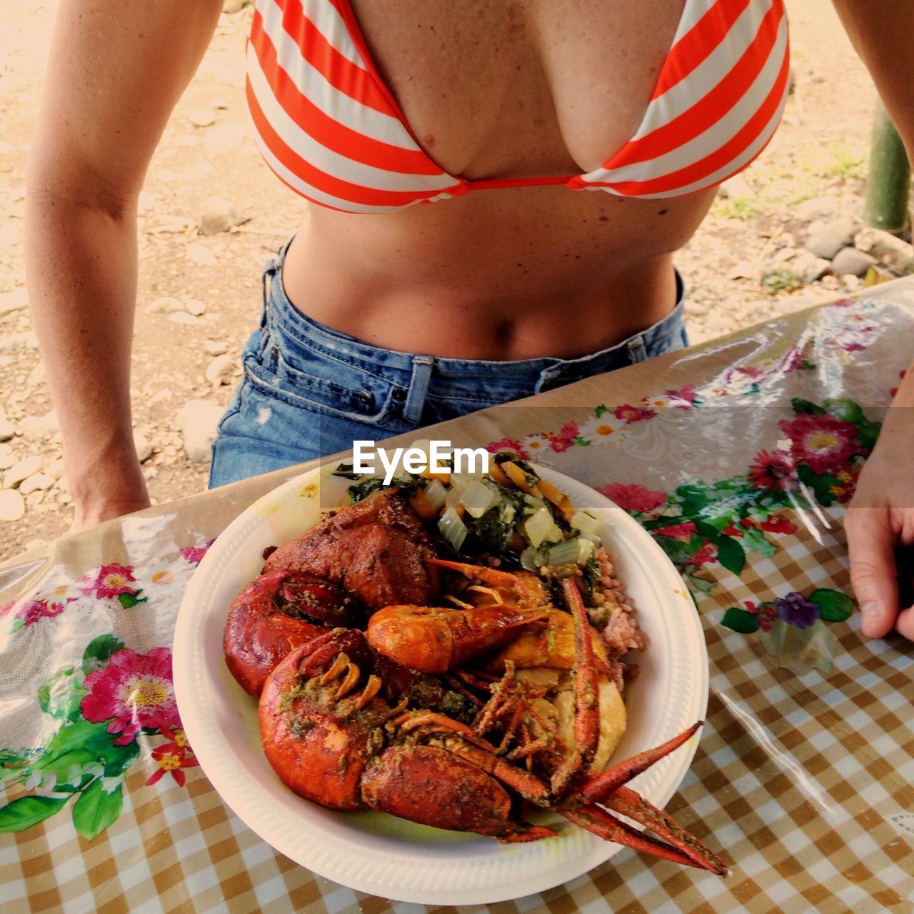 Midsection of woman in bikini top with cooked crayfish served on table