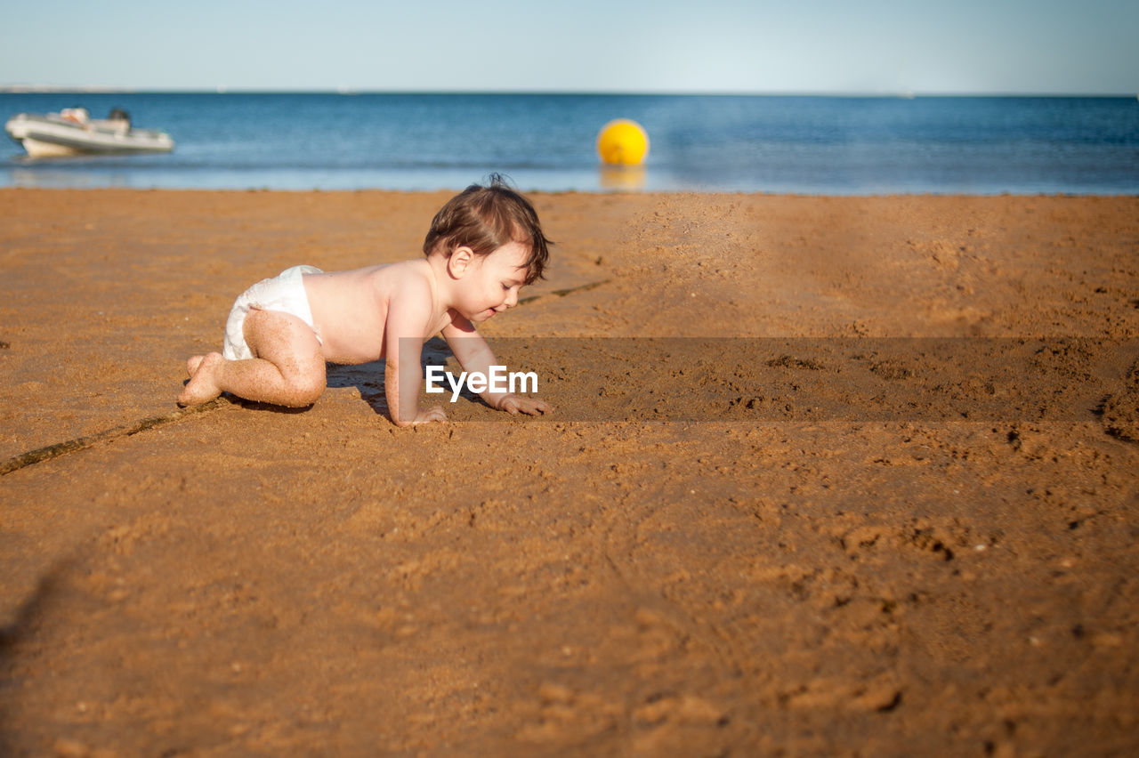 FULL LENGTH OF SHIRTLESS BOY ON SAND AT BEACH