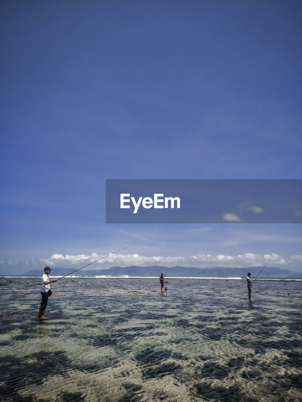 People angling while standing in sea against sky