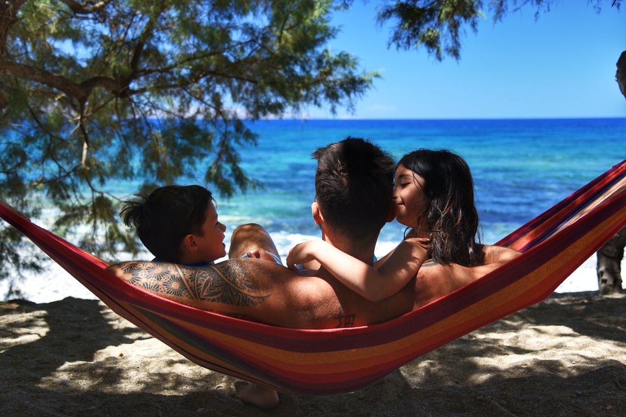 Rear view of father with children relaxing in hammock at beach