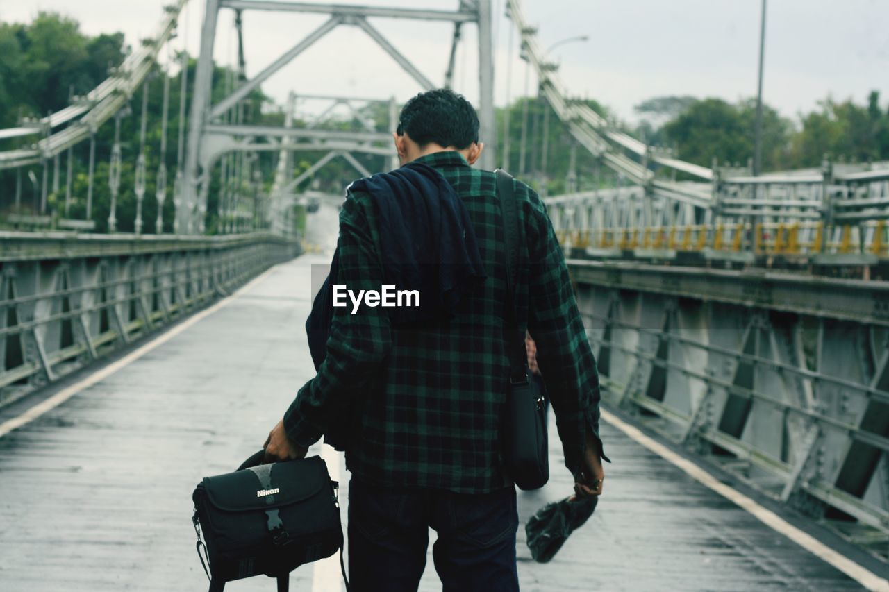 REAR VIEW OF MAN STANDING ON BRIDGE