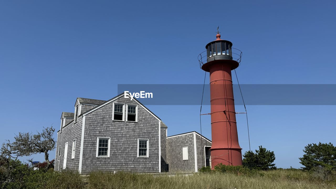 architecture, built structure, building exterior, lighthouse, building, tower, sky, house, guidance, nature, blue, clear sky, security, no people, plant, protection, observation tower, day, outdoors, tree, grass, low angle view, land, landscape, travel destinations
