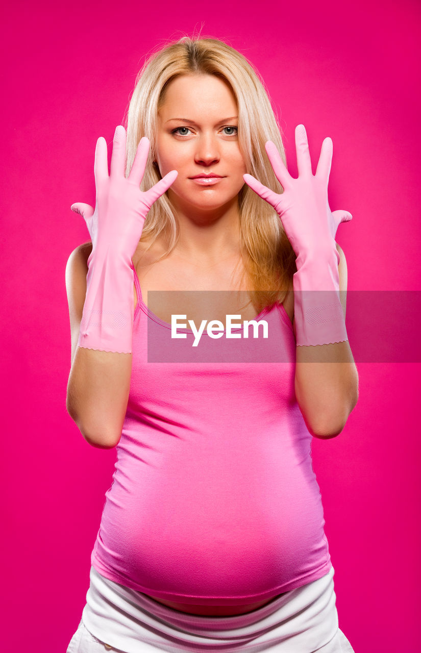 Portrait of pregnant woman exercising standing against pink background