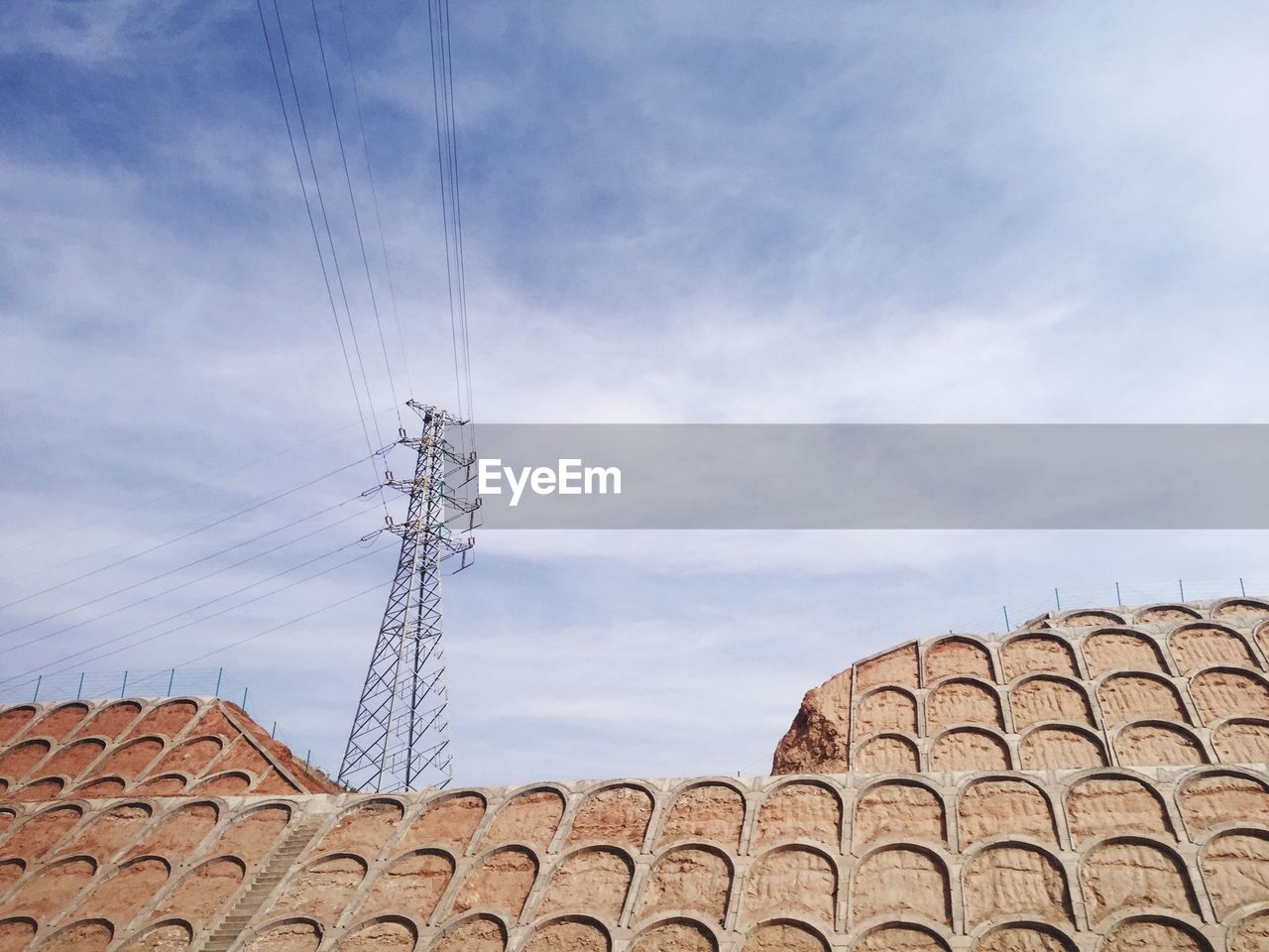 Low angle view of built structure and electricity pylon against sky