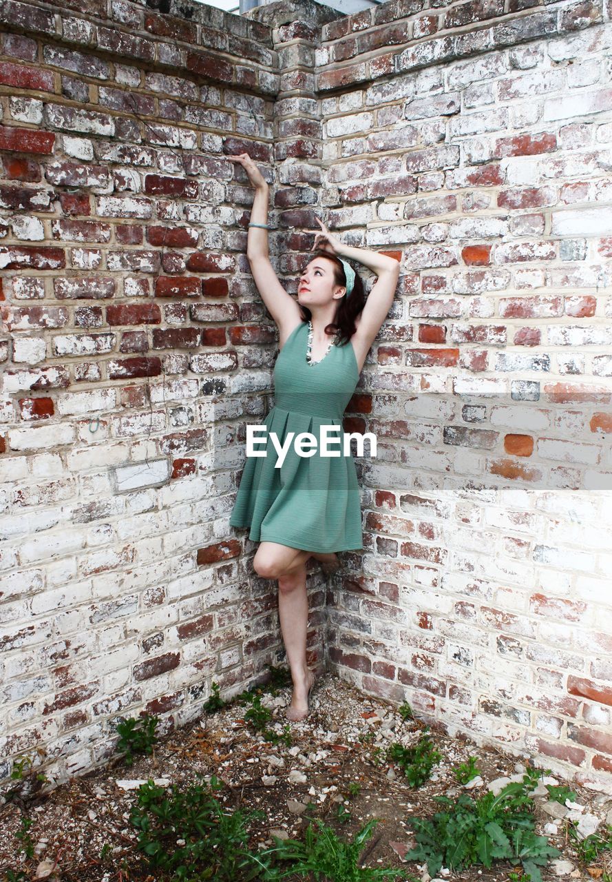 PORTRAIT OF YOUNG WOMAN STANDING ON BRICK WALL