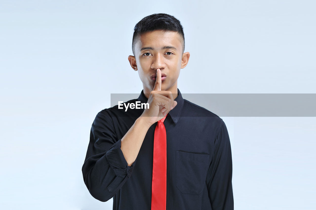 Young asian business man asking to be quiet with finger on lips. silence and secret concept
