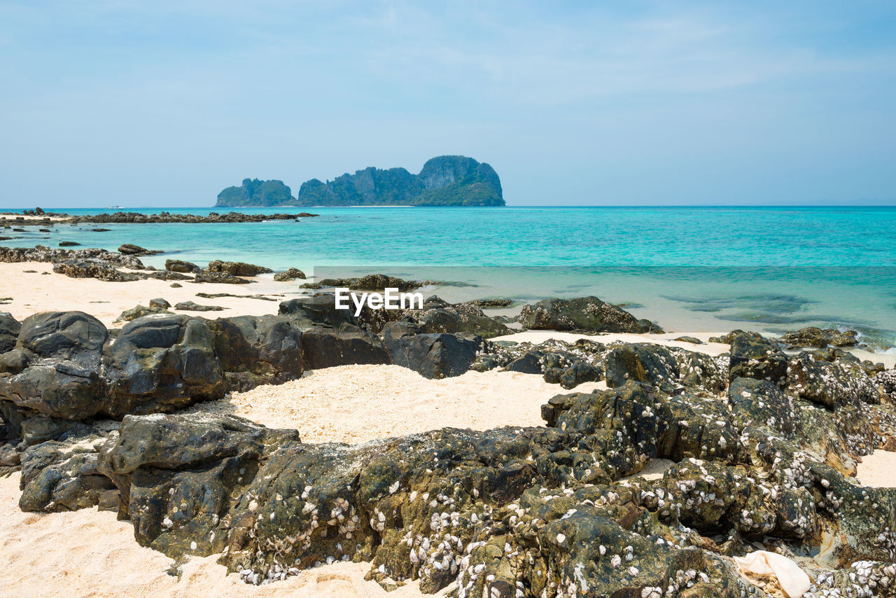 Tropical sea landscape with rocks at sand beach and rocky island at horizon