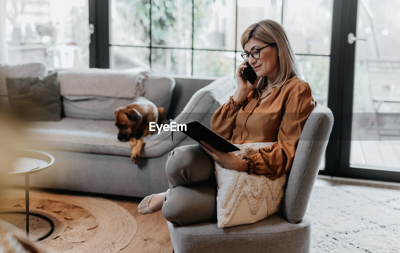 Businesswoman talking on phone while reading book at home