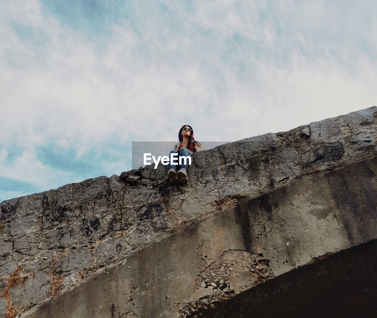 Low angle view of woman sitting on bridge against sky