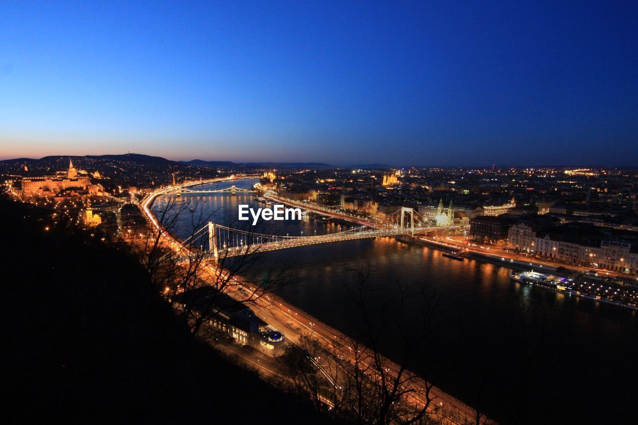 High angle view of bridge over river against clear blue sky in city at dusk