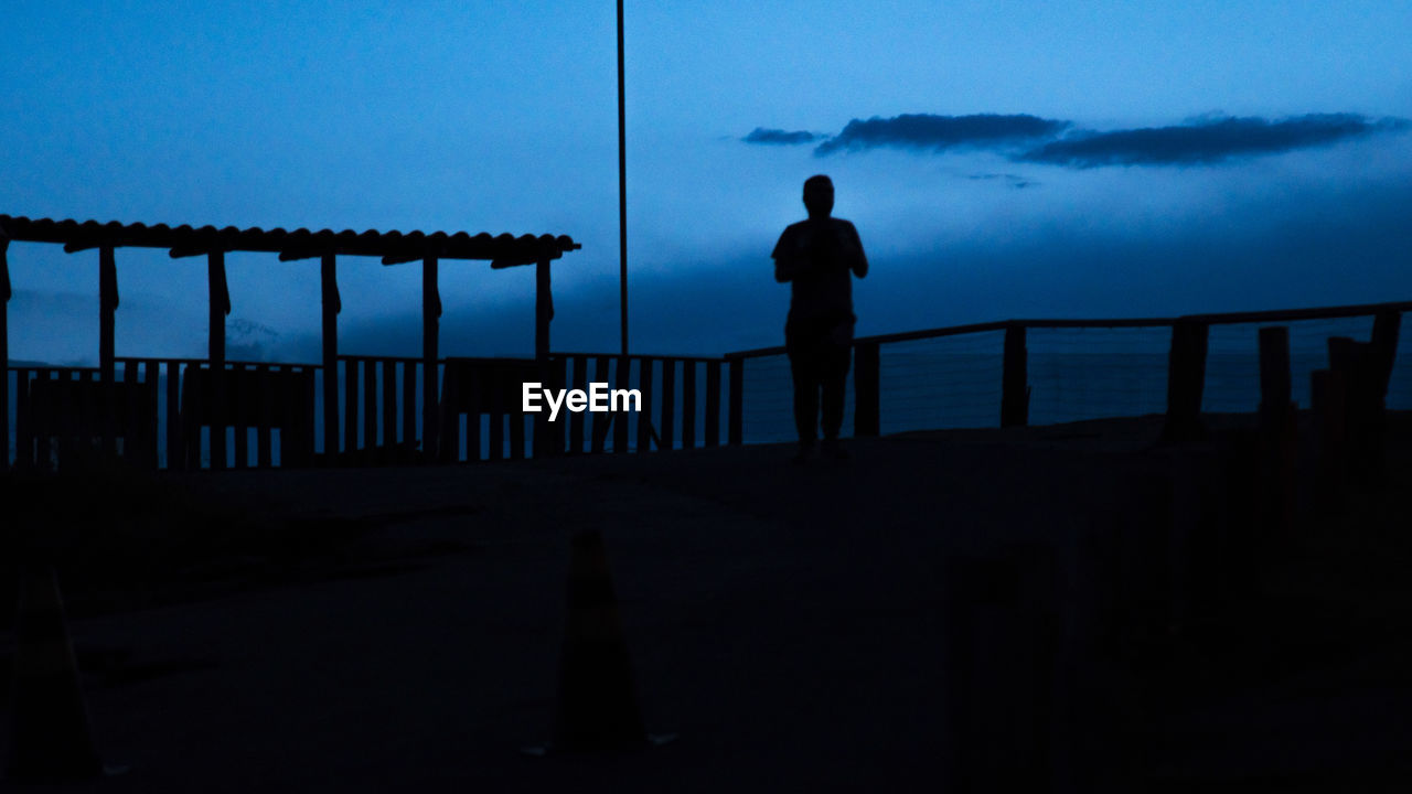 REAR VIEW OF SILHOUETTE MAN STANDING ON RAILING