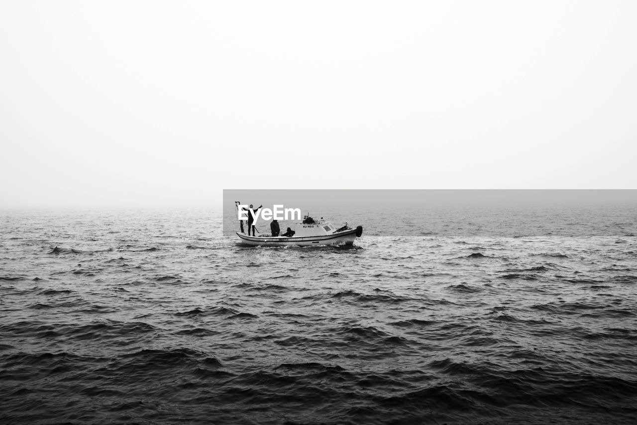 Men in sea against clear sky