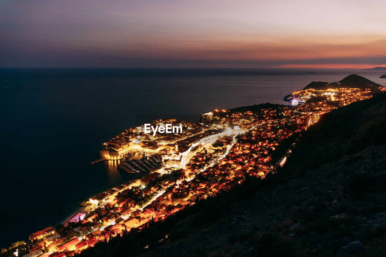 AERIAL VIEW OF ILLUMINATED CITY AGAINST SKY AT NIGHT