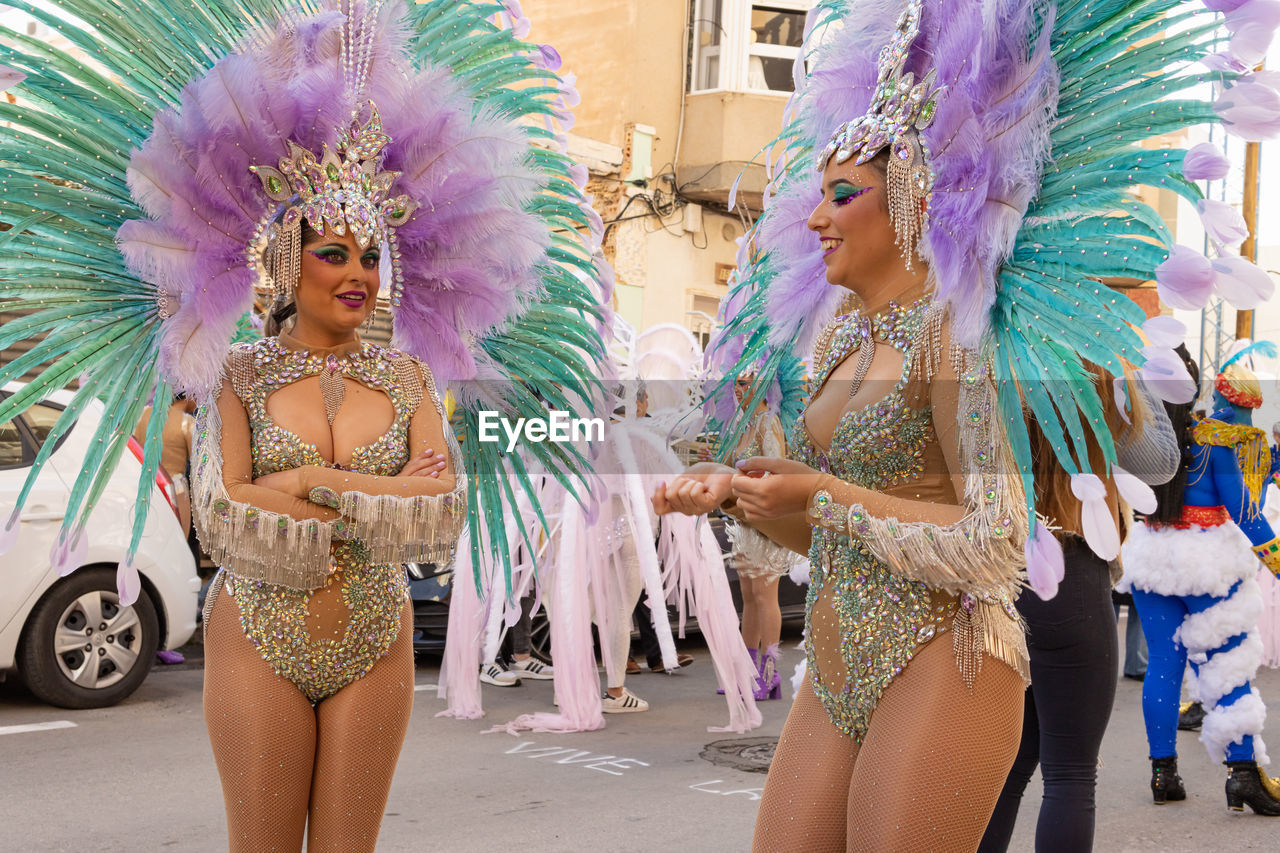 samba, feather, headwear, clothing, traditional clothing, arts culture and entertainment, carnival, dancing, showgirl, celebration, adult, performing arts, headdress, women, tradition, festival, costume, event, multi colored, young adult, fun, fashion, performance, traditional festival, glamour, enjoyment, performance art, city, portrait, three quarter length, smiling, emotion, street, two people, sports, outdoors, motion, happiness, lifestyles