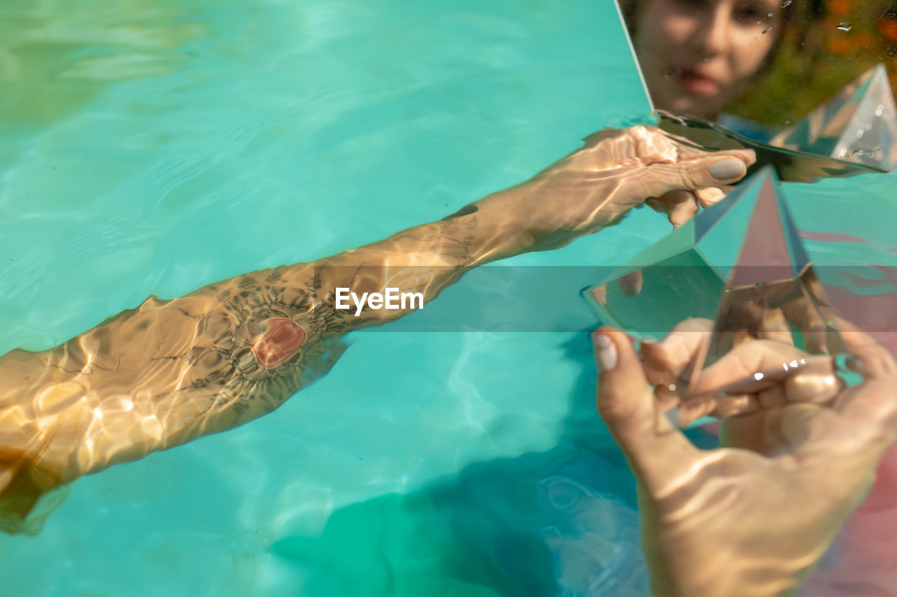 Reflection of woman in mirror holding prism while sitting in swimming pool