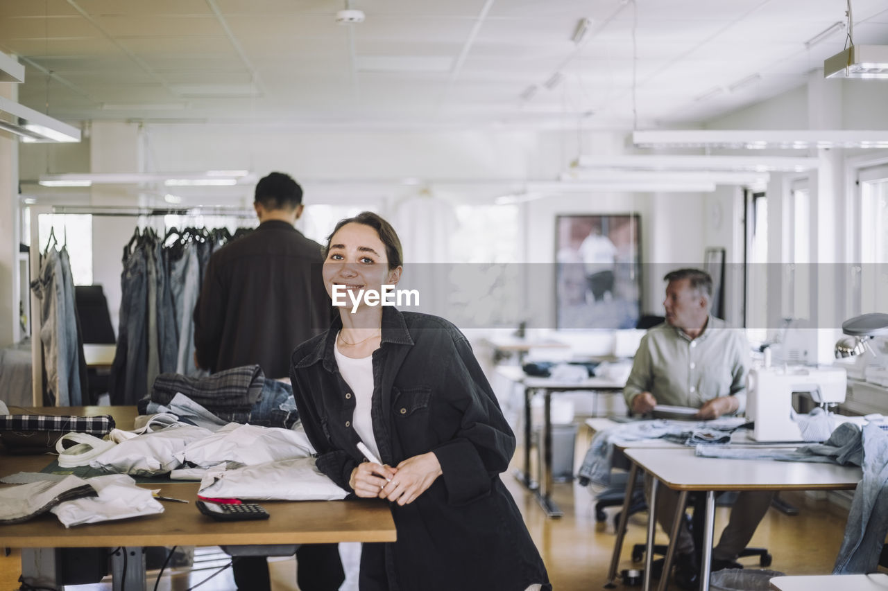 Portrait of smiling young fashion designer leaning on workbench at workshop