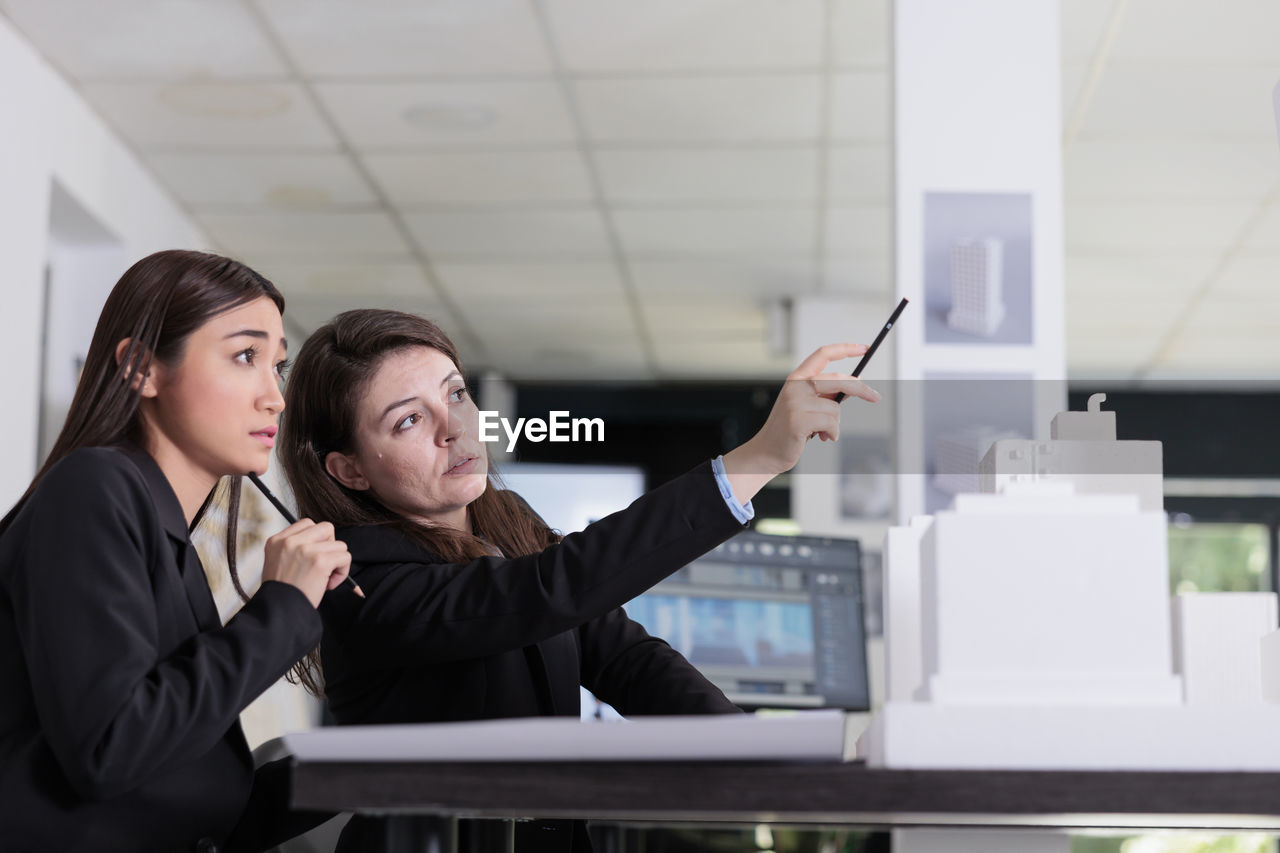 portrait of smiling young woman using mobile phone while standing in office