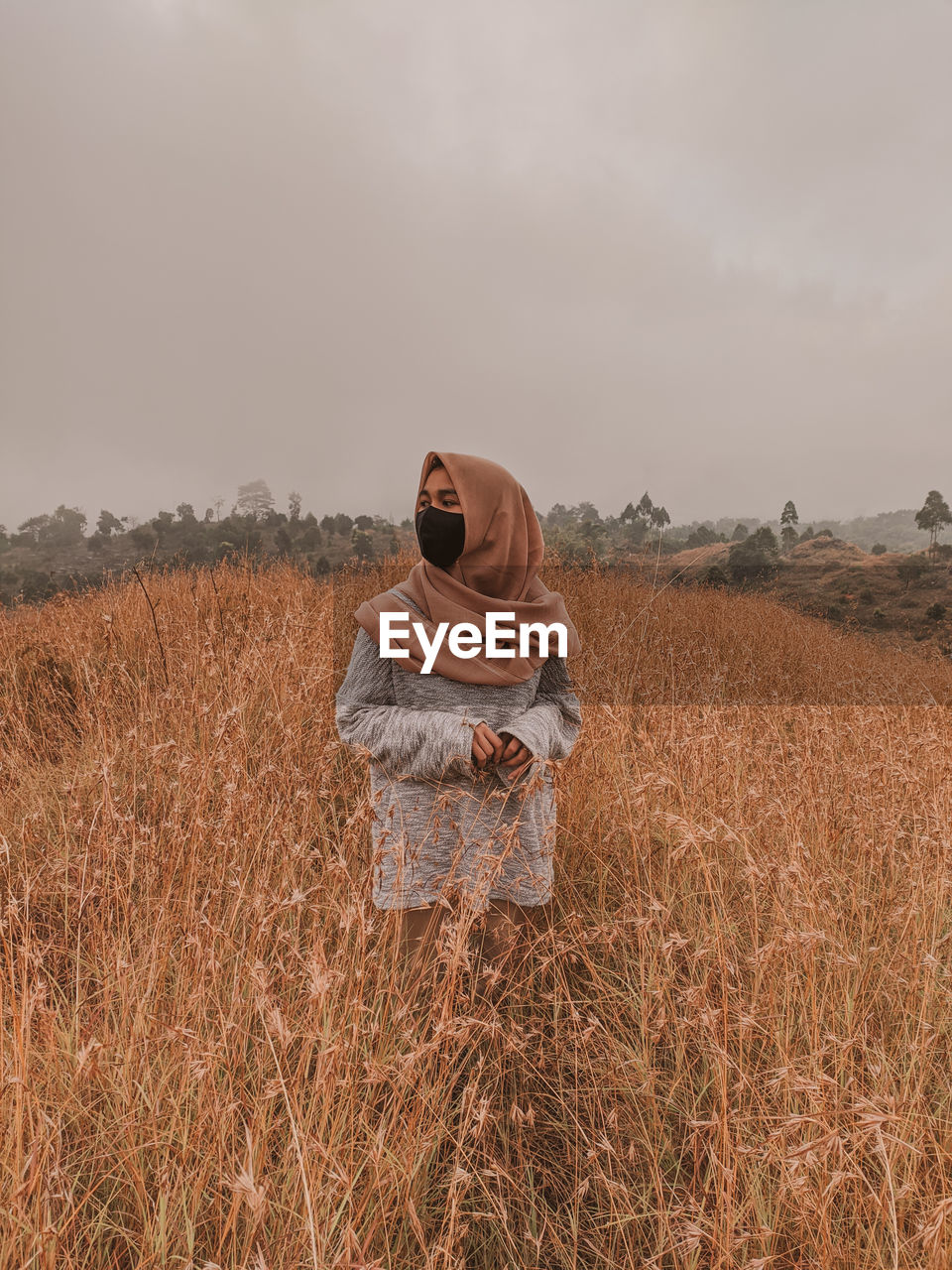 Woman wearing mask standing on field against sky