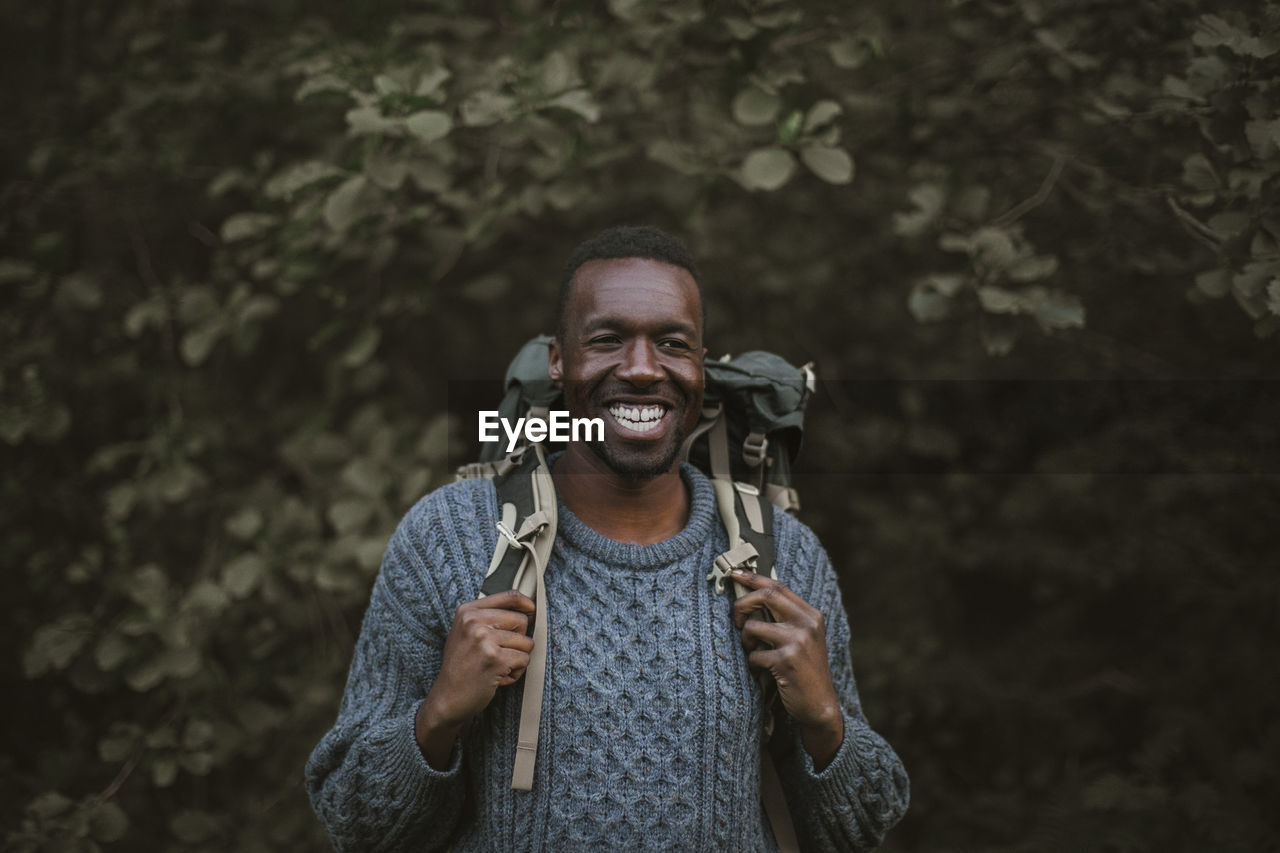 Smiling man with backpack standing in forest