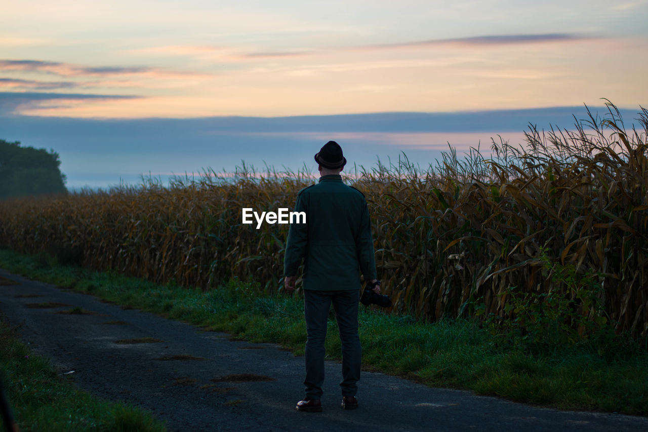 REAR VIEW OF MAN STANDING ON ROAD AGAINST SKY