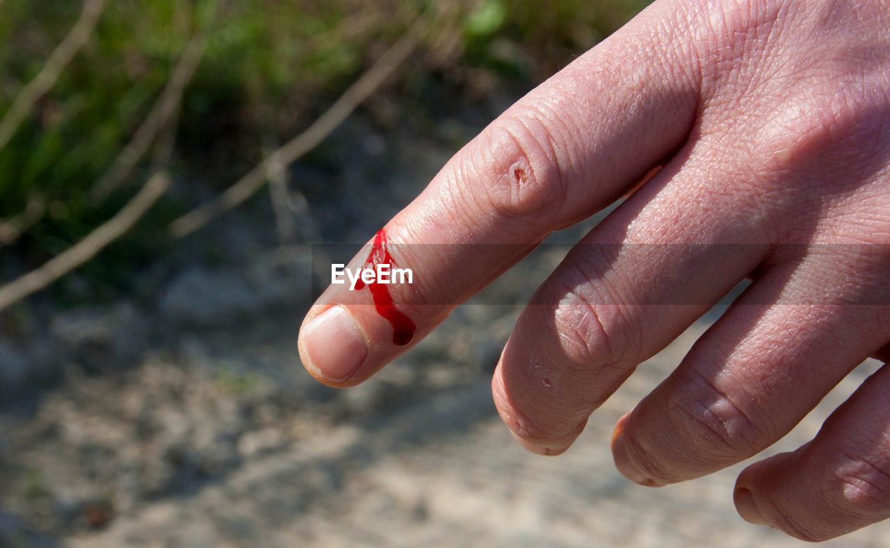 CLOSE-UP OF HAND HOLDING CIGARETTE OUTDOORS