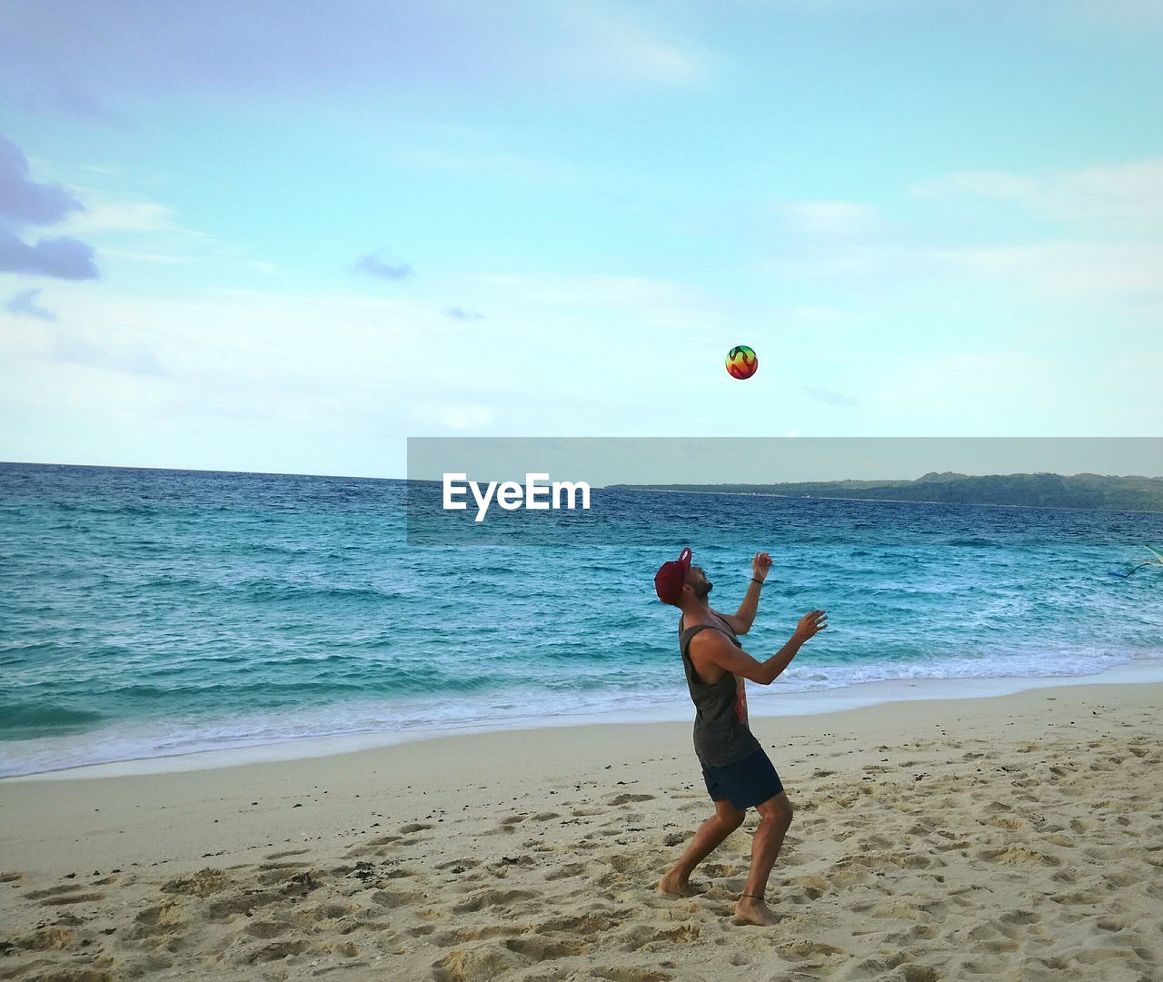 Side view of man playing with ball at beach against blue sky