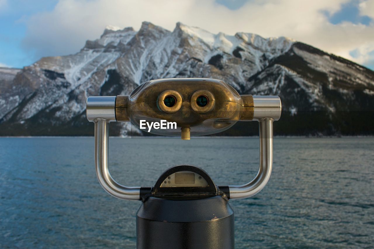 Close-up of coin-operated binoculars by sea against sky