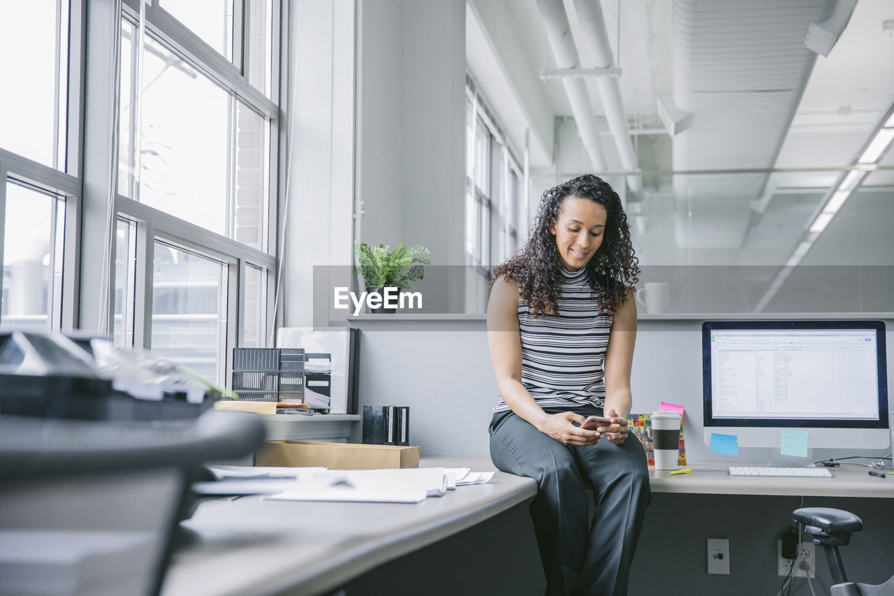 Businesswoman using mobile phone while sitting on desk in office