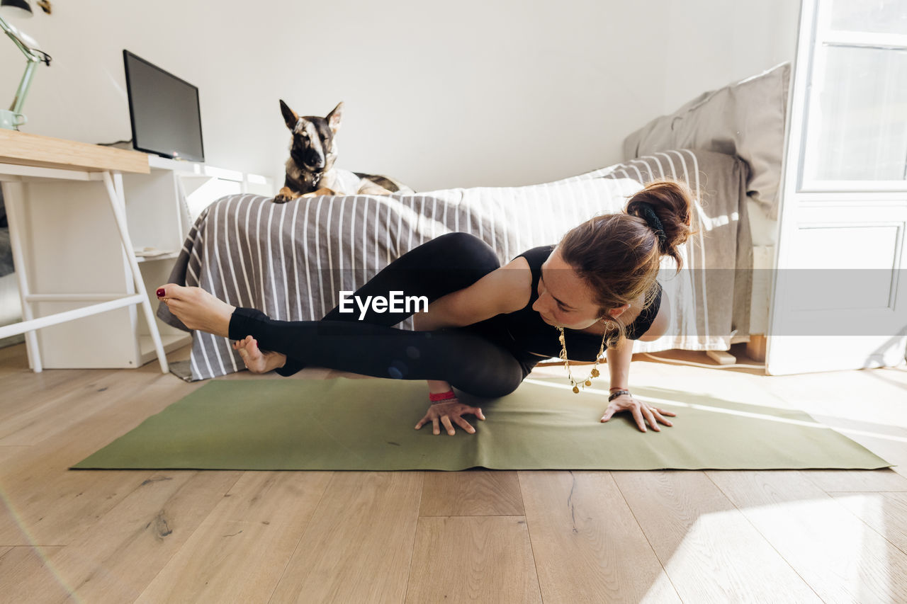 Woman practicing yoga on exercise mat in bedroom at apartment