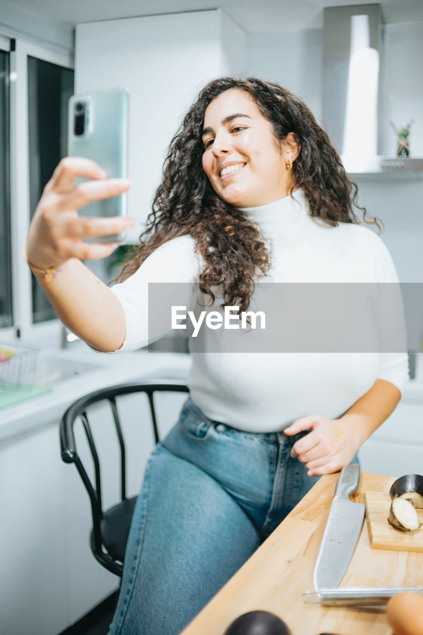 portrait of smiling young woman using mobile phone while sitting on table