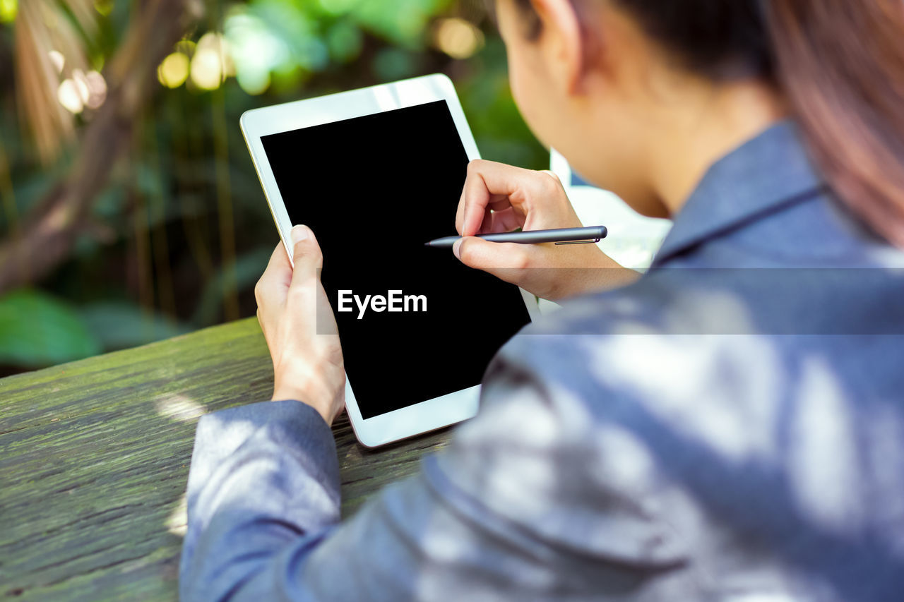 Midsection of woman using digital tablet on table while sitting outdoors