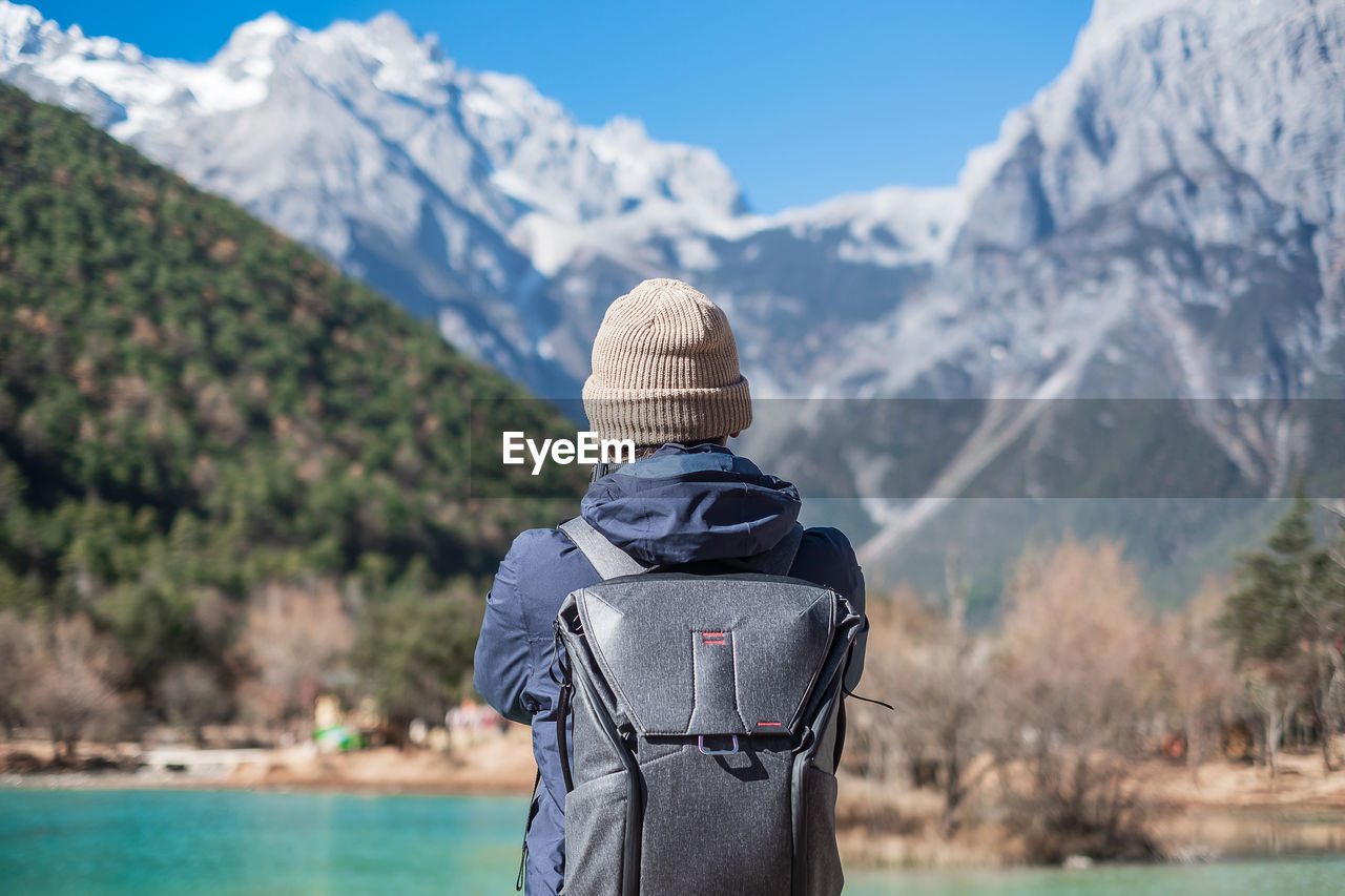 Rear view of man wearing backpack while standing against mountains during winter