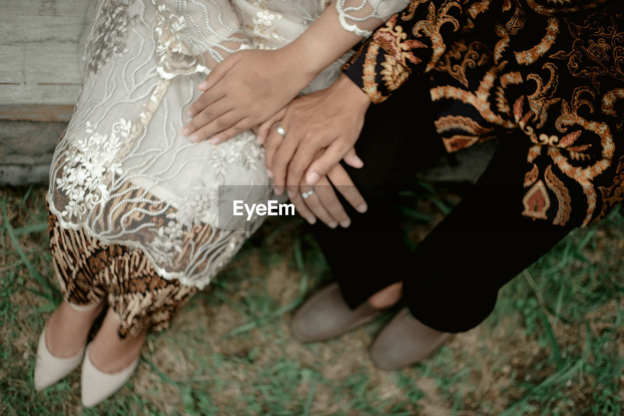 Low section of couple holding hands while siting outdoors