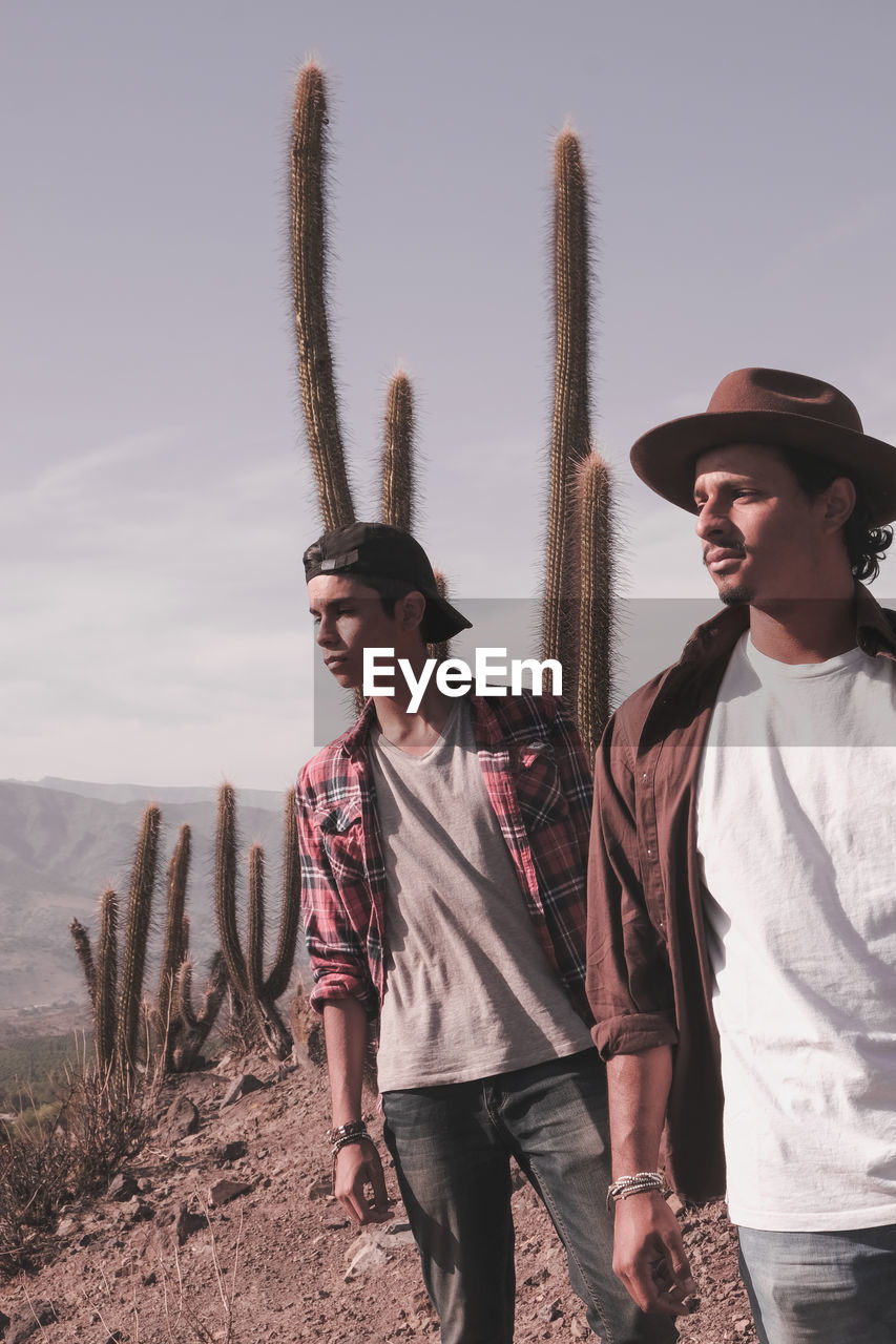 Young men looking away while standing against cactus on field