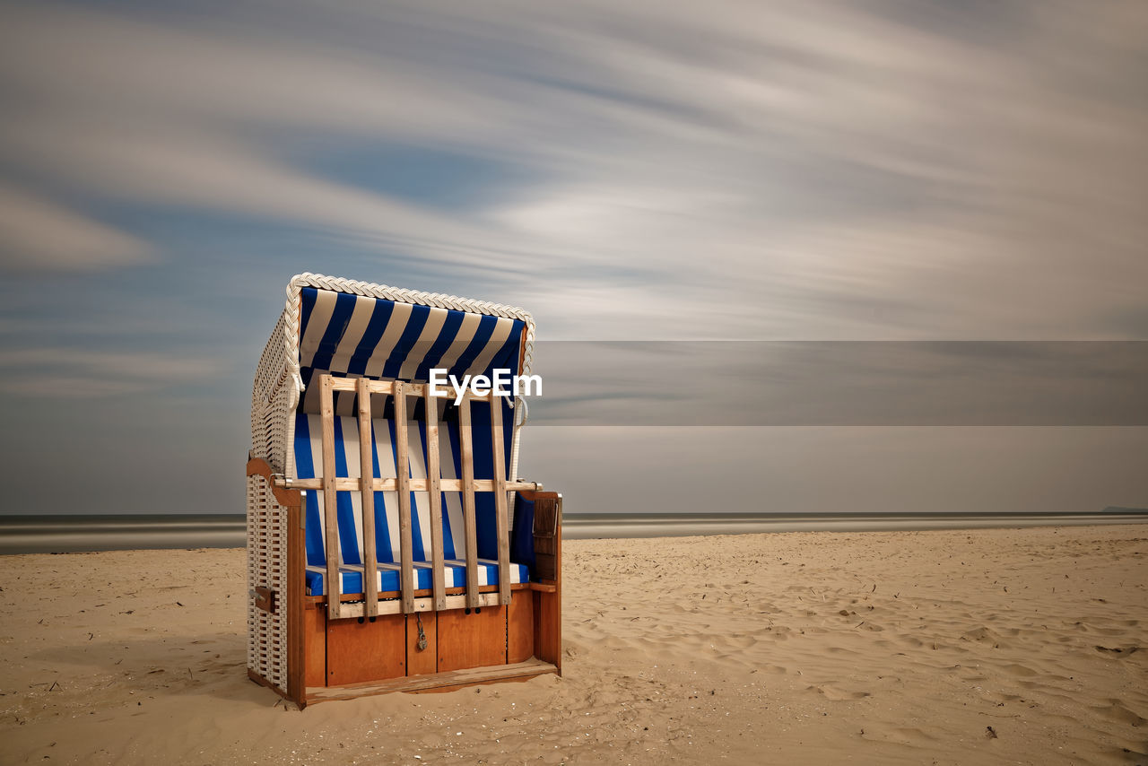 Hooded chair on beach against cloudy sky