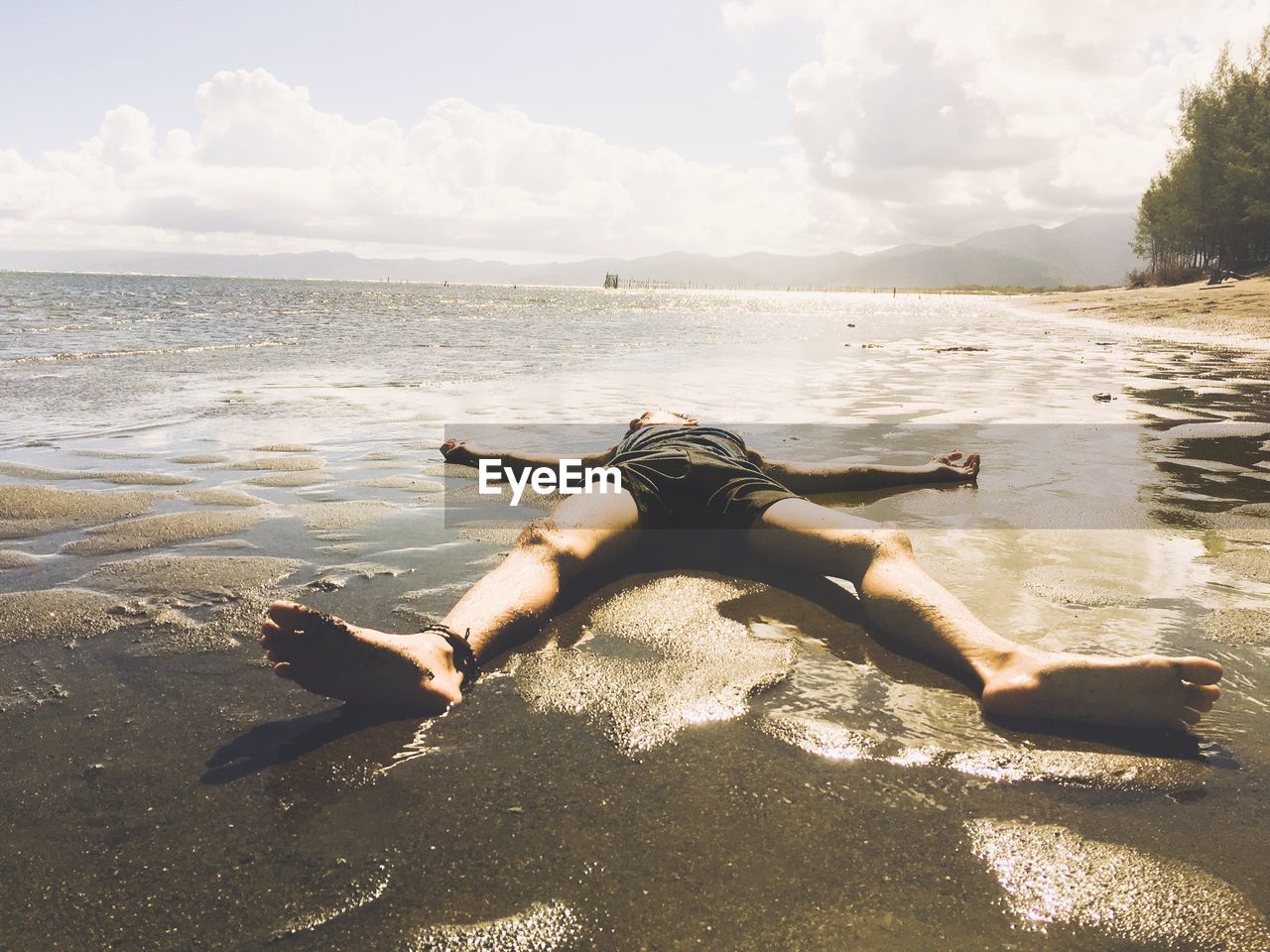 Full length of shirtless man lying at beach against sky