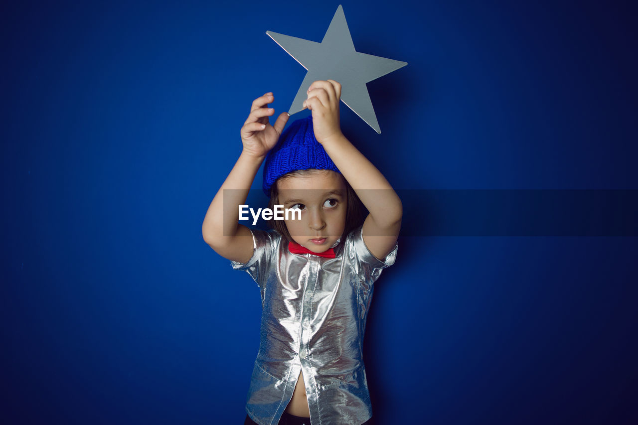 Christmas boy child holding a star in a silver shirt blue hat and red bow tie stands in the studio