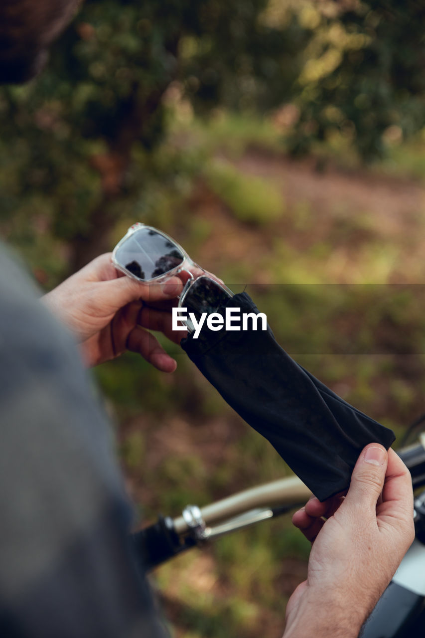 Cropped unrecognizable person hands taking off a dust bag a black sunglasses in nature green background