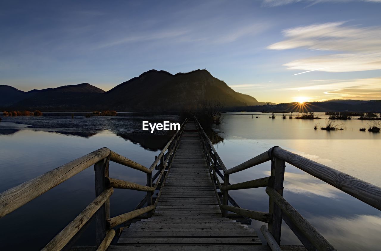 Wooden pier over lake against sky during sunset